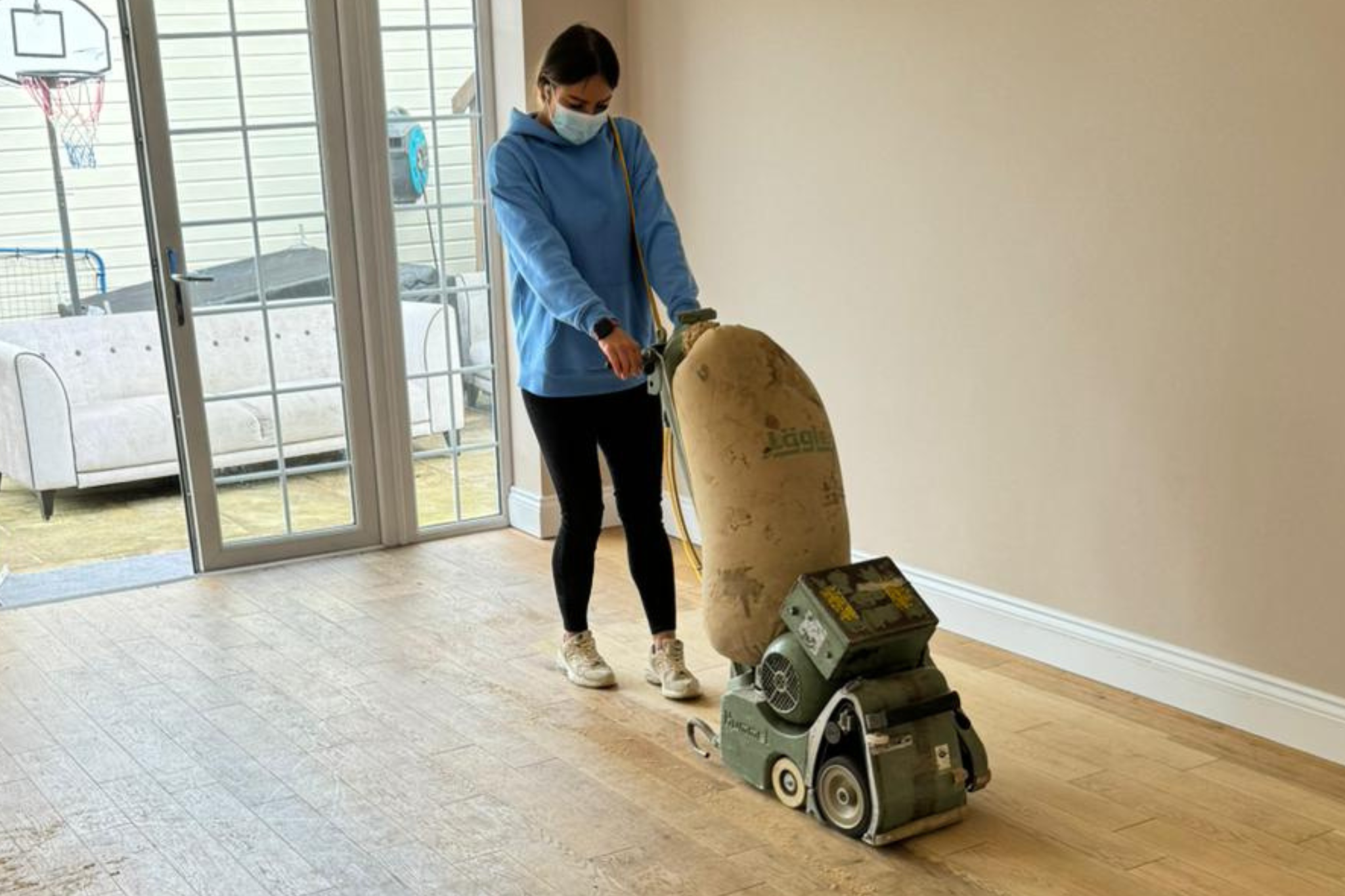 Technician performing Wood Floor Sanding in Surbiton on an engineered oak hardwood plank floor using a dust-extraction belt sander.