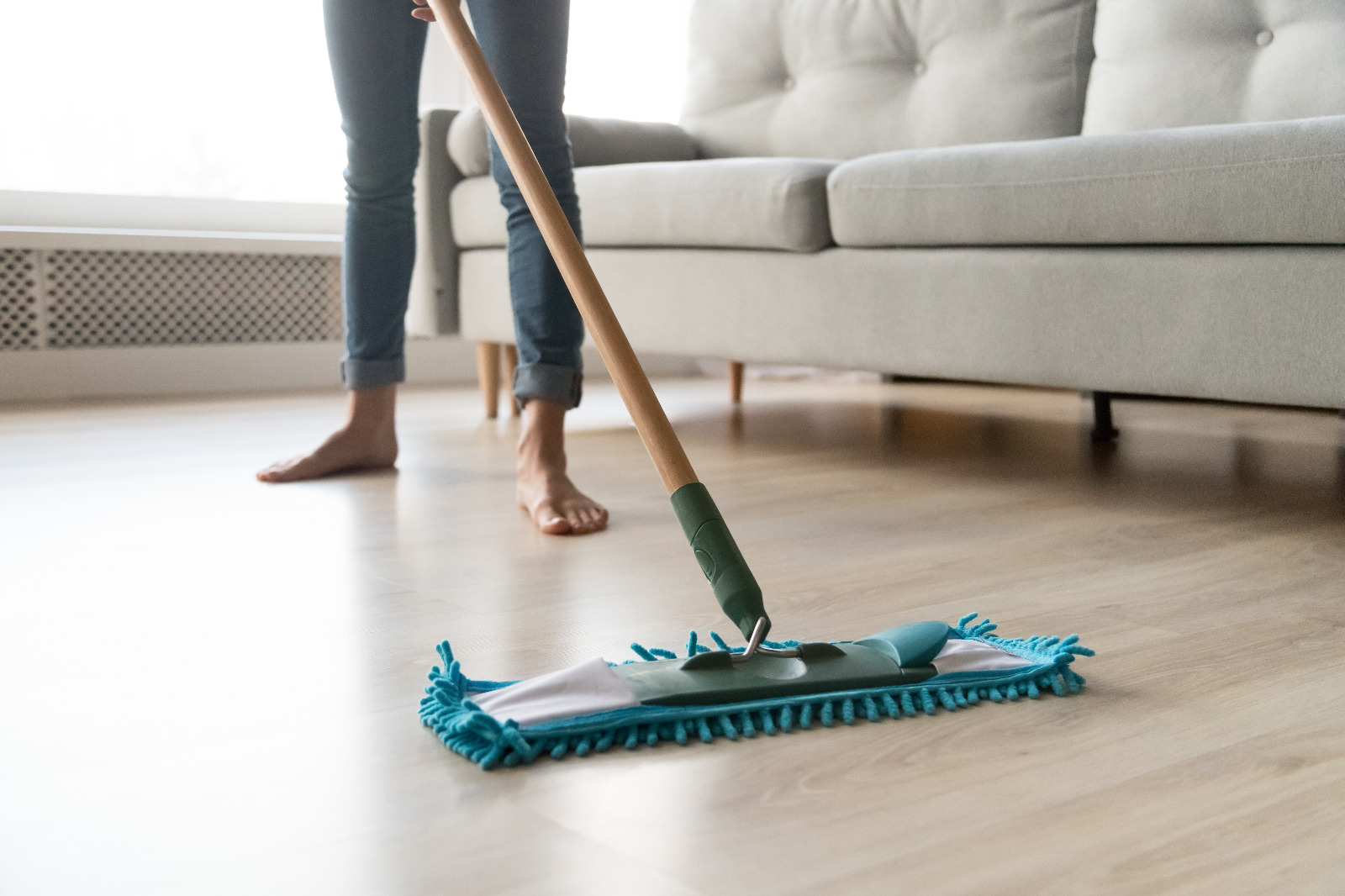 After Wood Floor Sanding in Surbiton, a homeowner uses a microfibre flat mop to clean a light oak engineered hardwood floor, maintaining the newly sealed surface.