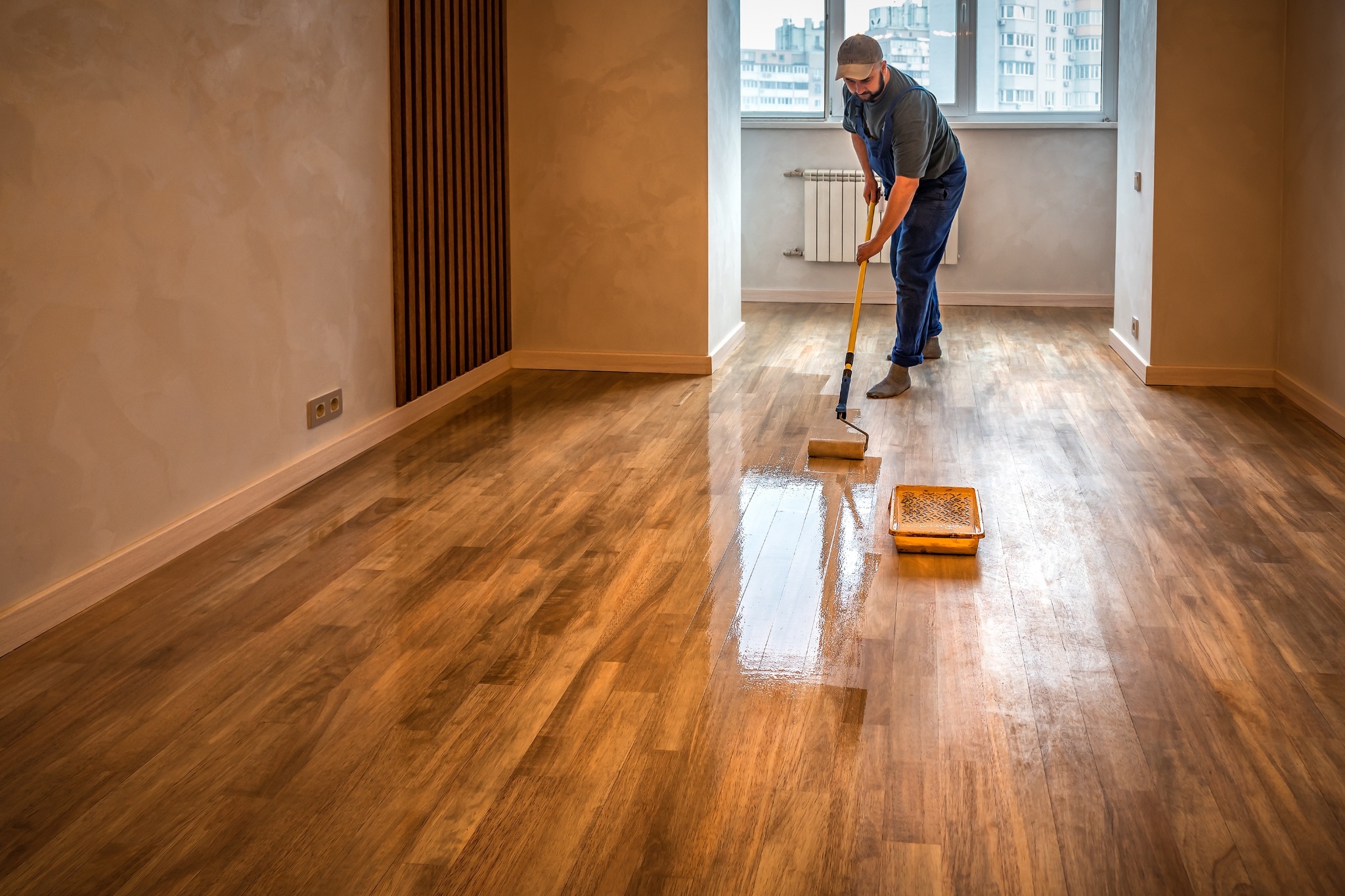 Technician applying protective finish after Wood Floor Sanding in Surbiton on an oak strip hardwood floor, using a pad applicator for a smooth, satin sheen.