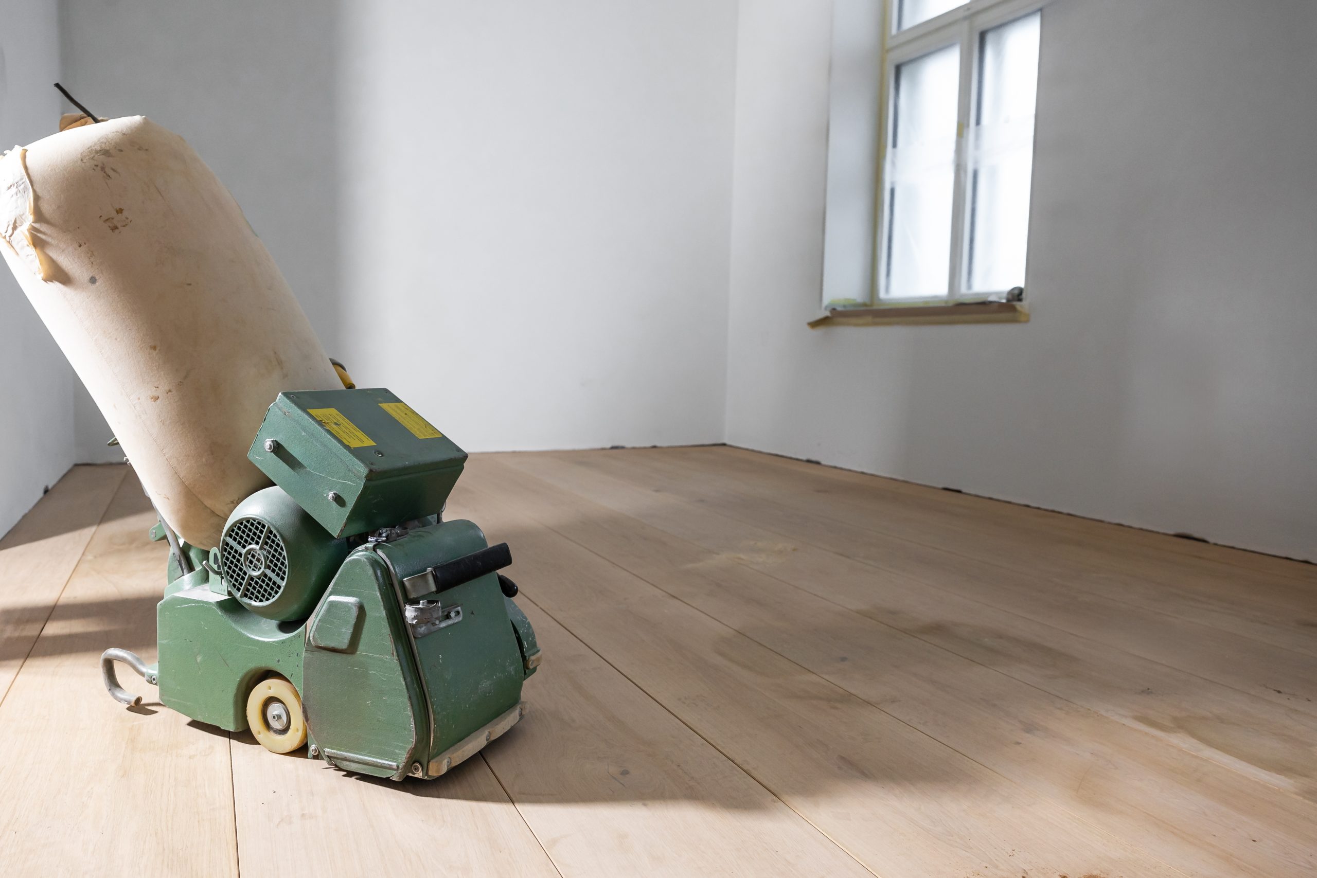 Wood Floor Sanding in Surbiton – Wide-Plank Oak Hardwood Floor (In Progress) Wood Floor Sanding in Surbiton on a wide-plank oak hardwood floor, shown mid-process with a belt sander and dust bag.