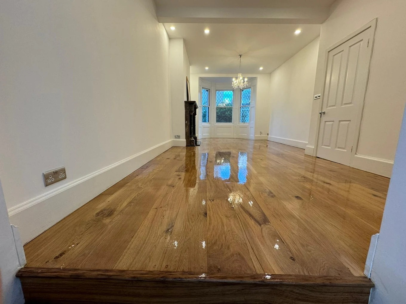 Hardwood Floor Sanding in Surbiton — engineered oak plank living/dining room newly sanded and coated to a high-gloss finish, showing clear reflections and rich grain.