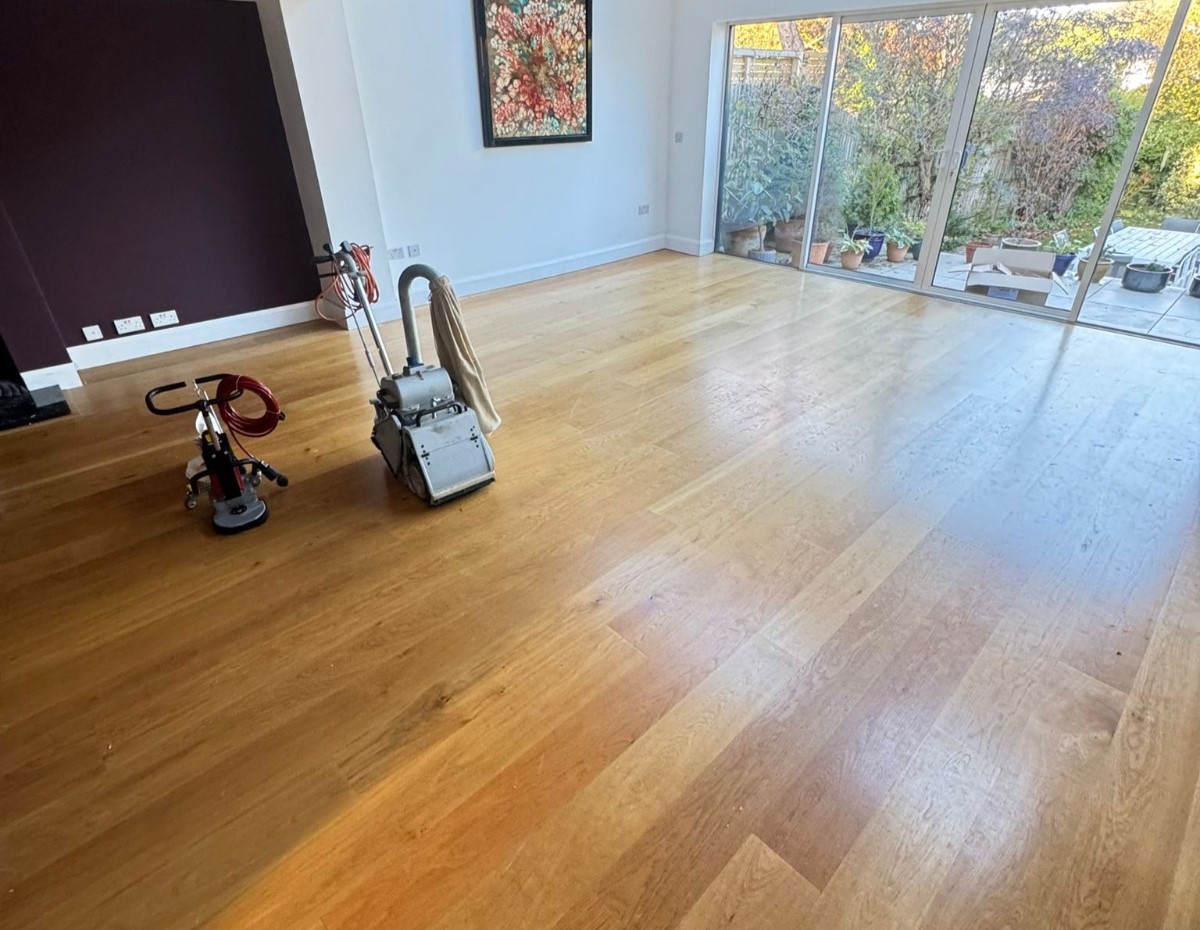 Hardwood Floor Sanding in Surbiton — engineered oak wide-plank living room mid-sanding, with belt sander and buffer preparing the dull surface for refinishing.