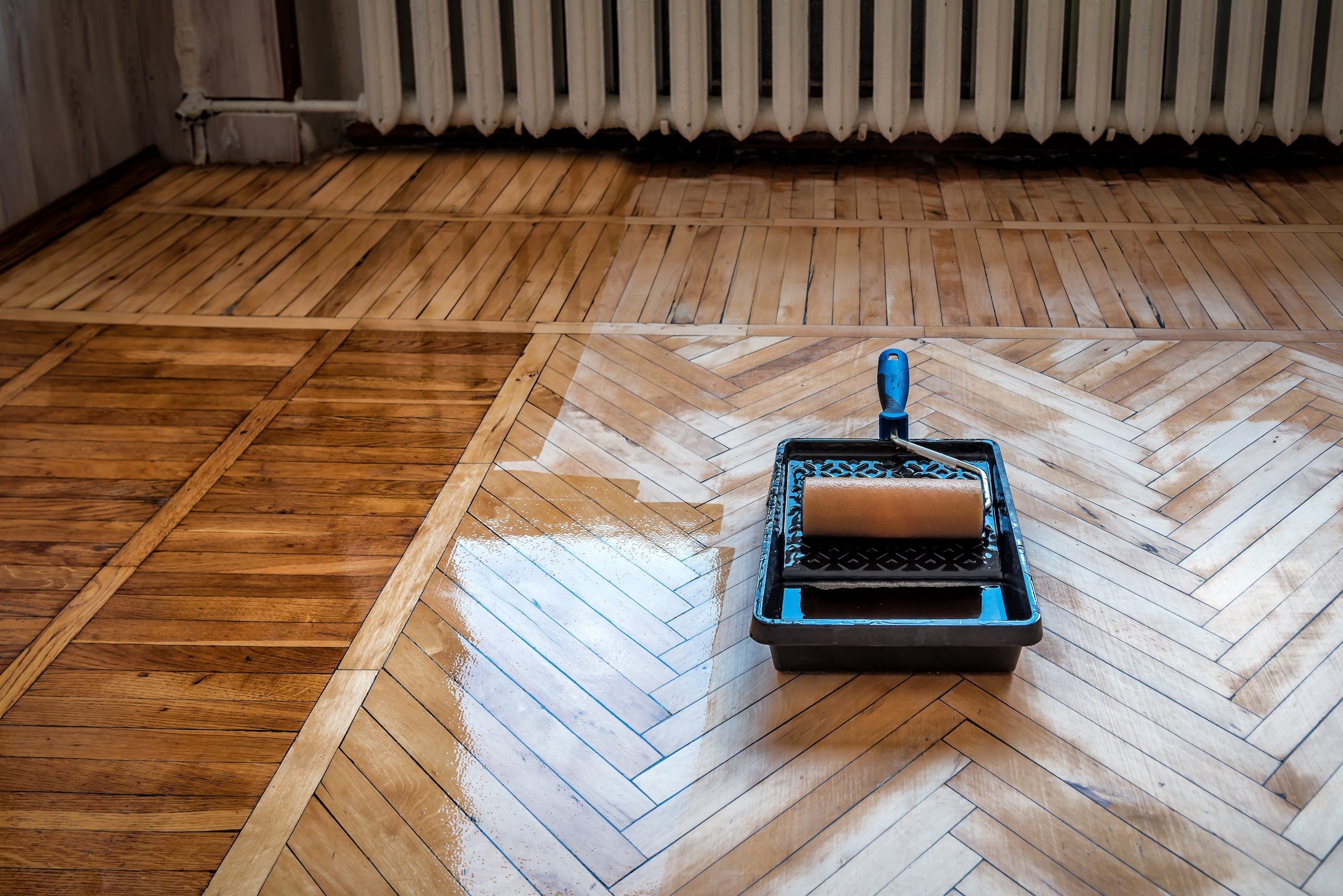 Hardwood Floor Sanding in Surbiton — oak herringbone parquet freshly sanded and being lacquered with a roller tray, highlighting the crisp chevron pattern and wet-edge sheen.