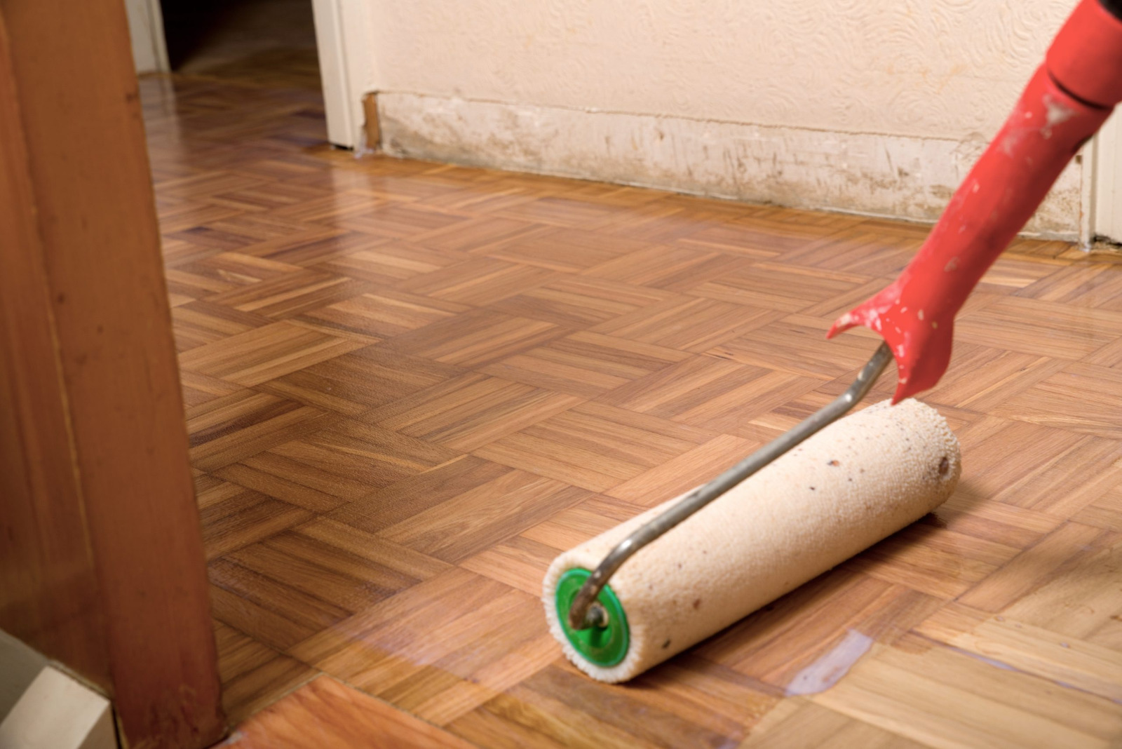 Wood Floor Sanding in Surbiton on an oak herringbone parquet floor, with a roller applying clear lacquer to the freshly sanded timber surface.